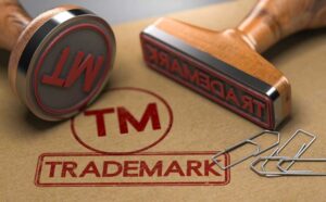 3D illustration of two rubber stamps with the word trademark and the symbol TM over brown paper background. Trade-mark Registration Concept